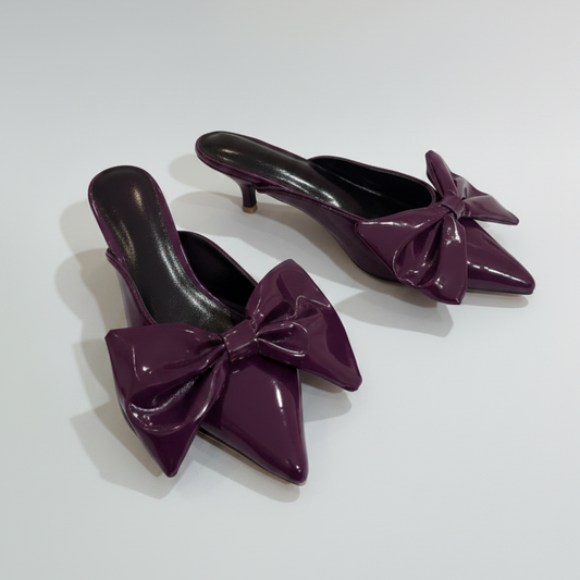 Black patent leather high heels with bow details on a white background