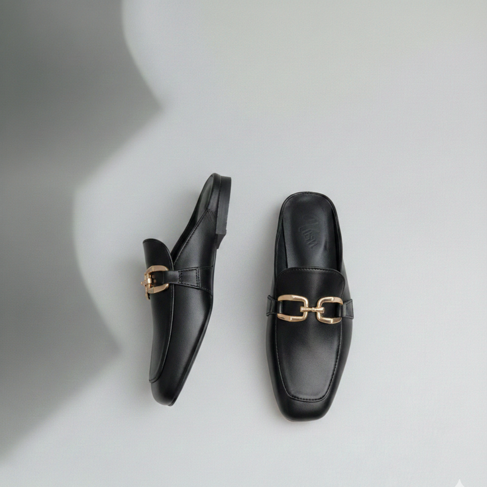 Black loafers with gold buckles on a light gray background