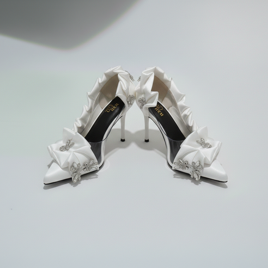 Pair of white high-heeled shoes with decorative bows on a light gray background