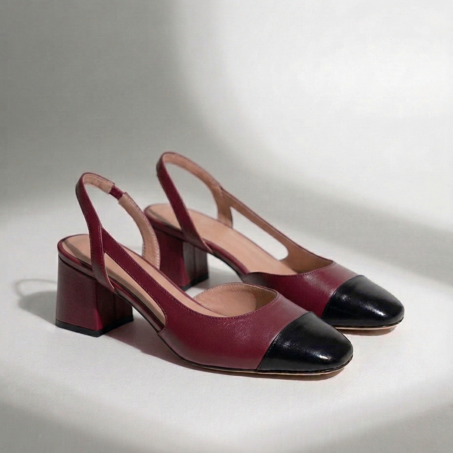 Pair of maroon and black high-heeled shoes on a light gray background