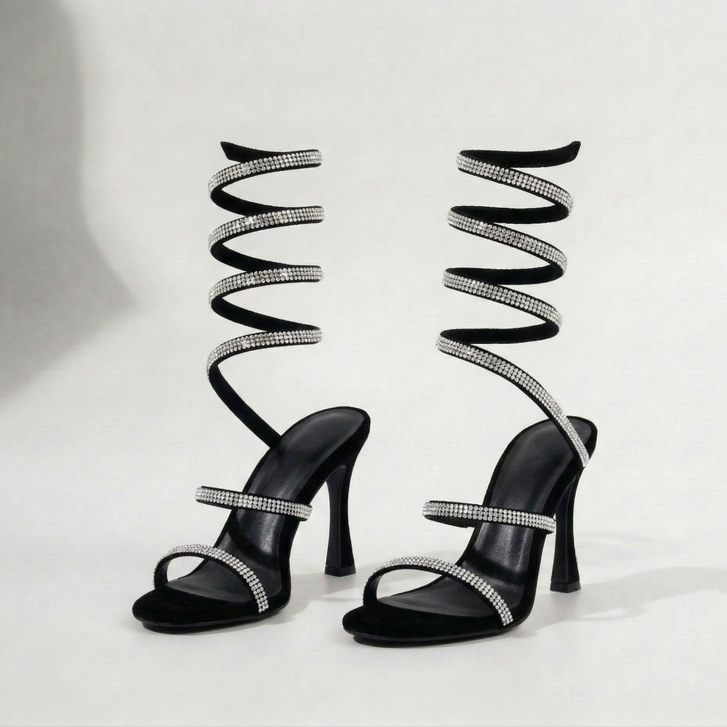 Black high-heeled sandals with spiral designs and rhinestone straps on a white background