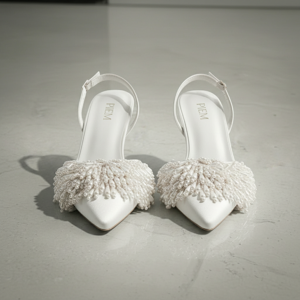 White high-heeled shoes with pearl embellishments on a gray surface